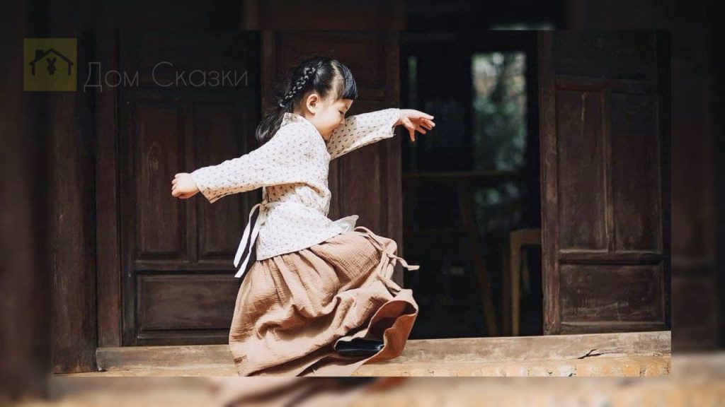 Сила улыбки, азиатская девочка размашисто шагает по улице в длинной пышной юбке.