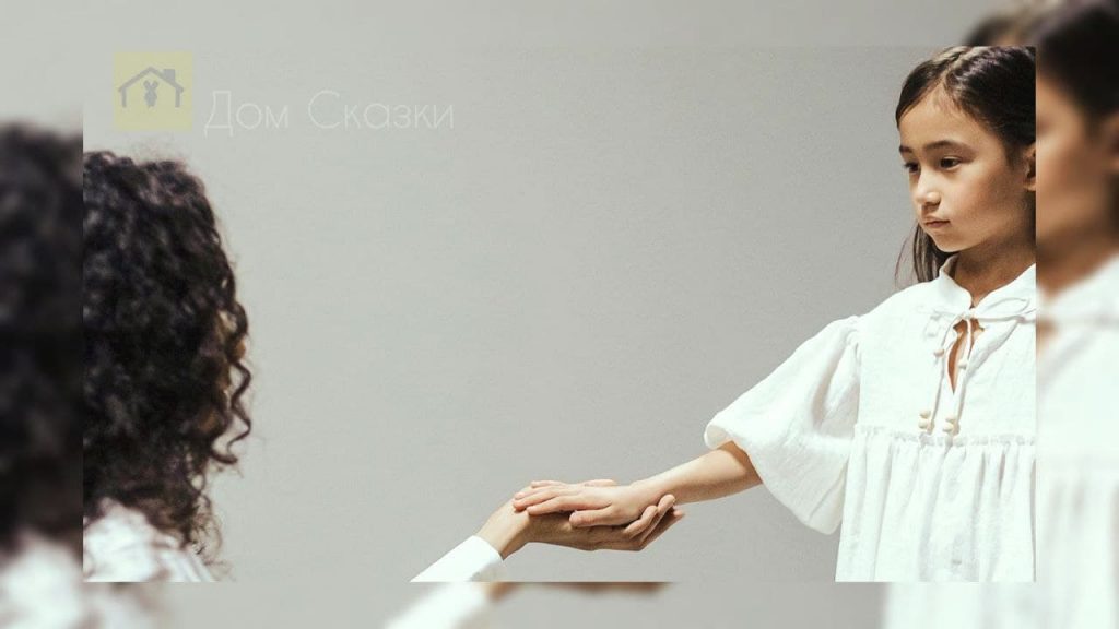 Темноволосая азиатская девочка в белой одежде протягивает руку темноволосой женщине.