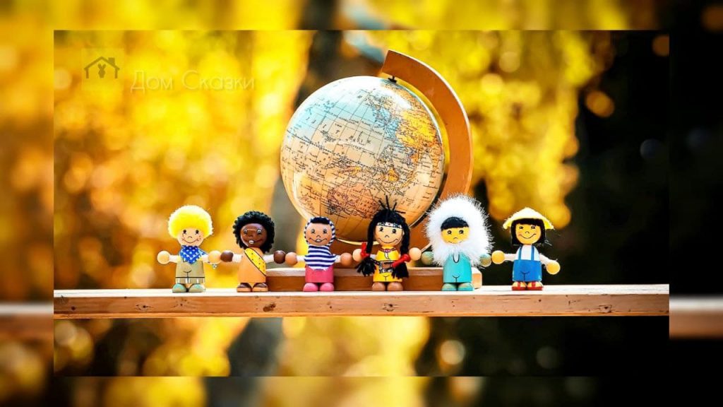 На деревянной дощечке стоят фигурки людей разной национальности, на заднем плане глобус.