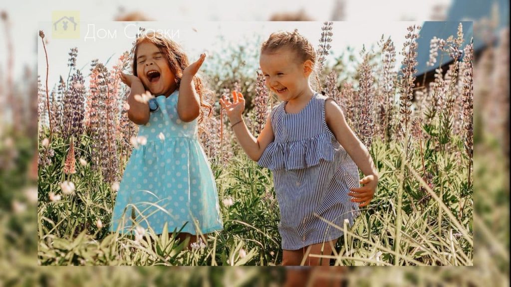 Две маленькие девочки в летних платьицах идут по полю усечнному цветами и весело смеются.