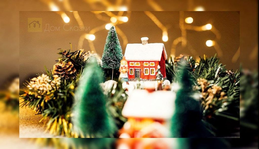 Маленький рождественский домик в окружении елей и шишек, в форме декорации.