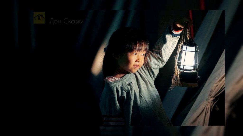Азиатская девочка держит уличный фонарик в руке и смотрит сквозь темноту.