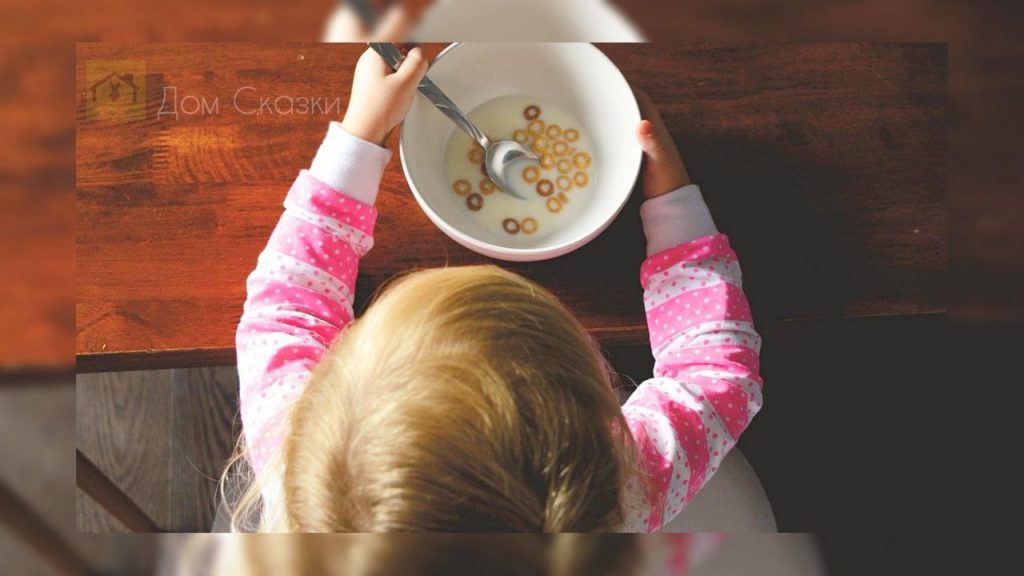 вид сверху на макушку девочкт со светлыми волосами, которая сидит за столом с тарелкой хлопьев с молоком