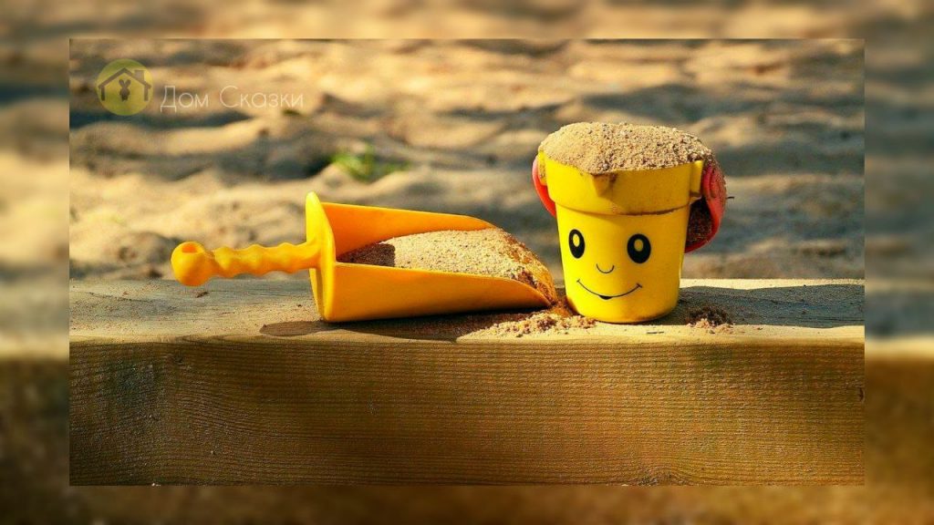 Сам такой, на картинке песочница, на боковинке песочницы стоит жёлтое ведёрко полное песка и жёлтая лопатка.