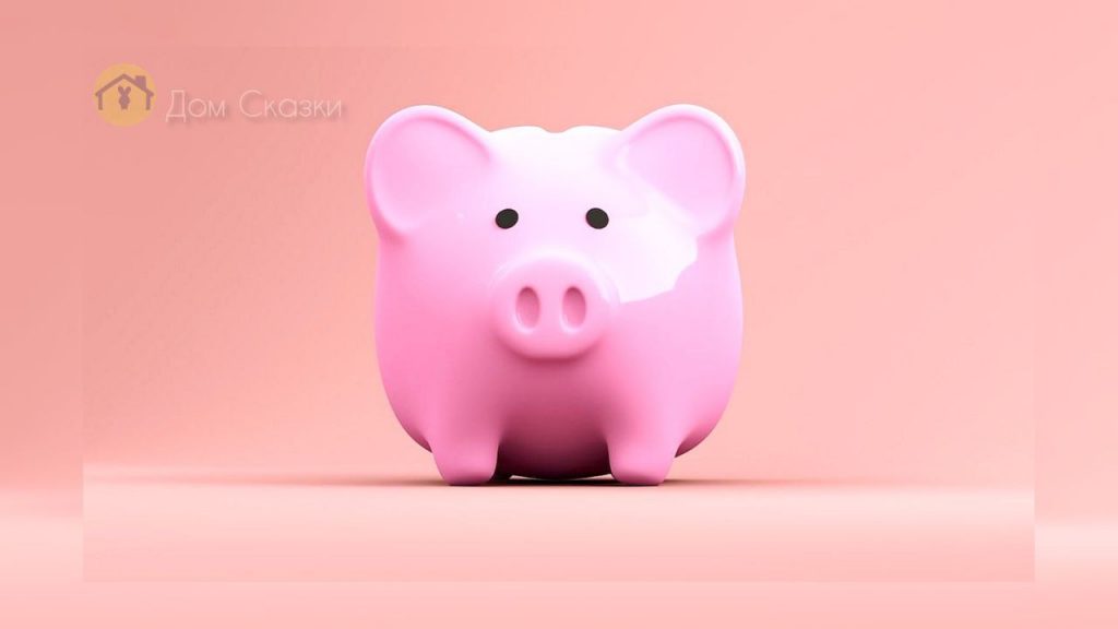 Розовая маленькая фарфоровая свинка-копилка стоит на нежном розовом фоне.